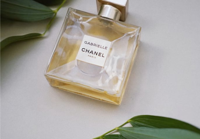 Gabrielle Chanel bottle laying flat on a table with green leaves above and below it